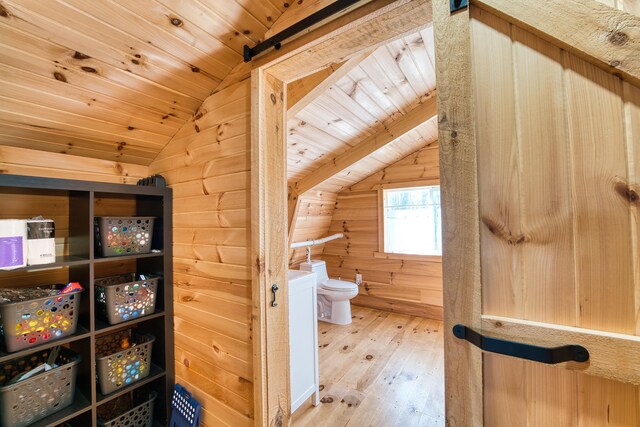 bathroom with hardwood / wood-style flooring, toilet, lofted ceiling, and wooden walls