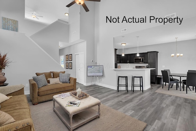 living room with a high ceiling, ceiling fan with notable chandelier, and dark wood-type flooring