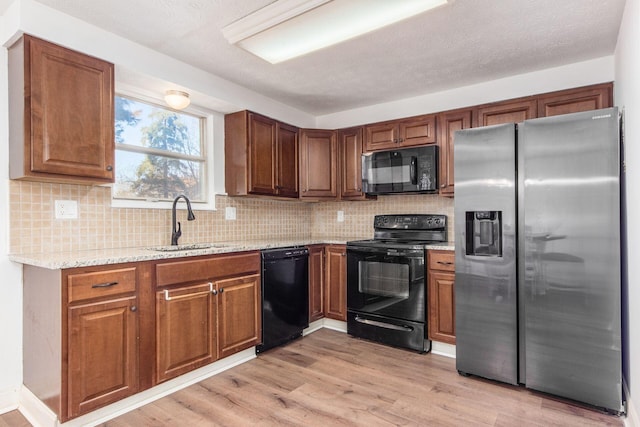 kitchen with backsplash, light stone counters, sink, black appliances, and light hardwood / wood-style flooring