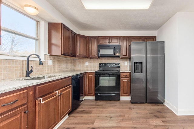 kitchen featuring sink, light stone counters, backsplash, black appliances, and light wood-type flooring