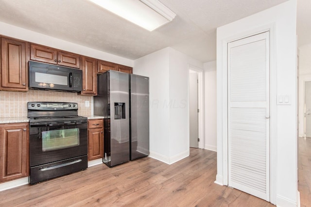 kitchen featuring backsplash, black appliances, light wood-type flooring, a textured ceiling, and light stone counters