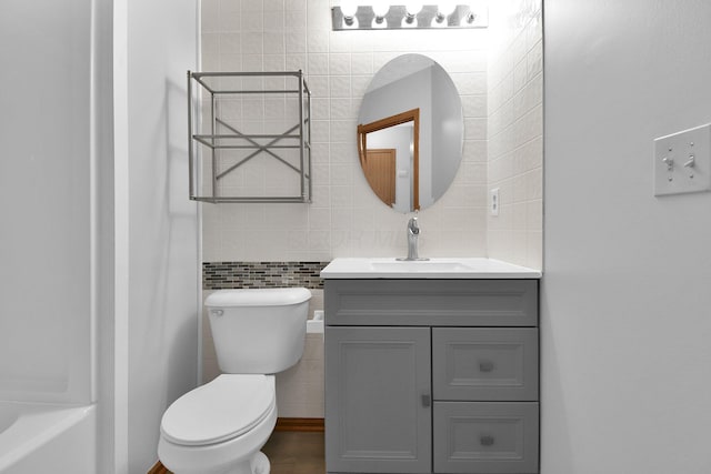 bathroom with a bathtub, vanity, tile walls, and toilet