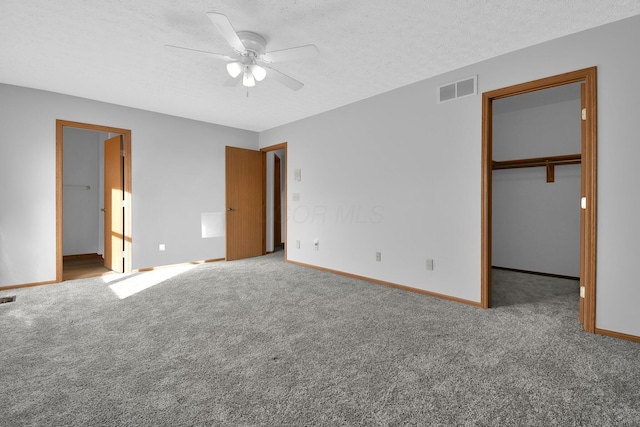 unfurnished bedroom featuring a spacious closet, ceiling fan, carpet floors, a textured ceiling, and a closet