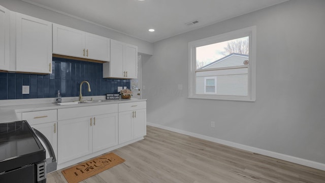 kitchen featuring sink, light wood-type flooring, tasteful backsplash, white cabinetry, and range