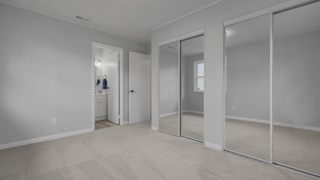 unfurnished bedroom featuring multiple closets, ensuite bathroom, and light carpet