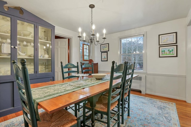 dining area with radiator heating unit, light wood-type flooring, lofted ceiling, and an inviting chandelier