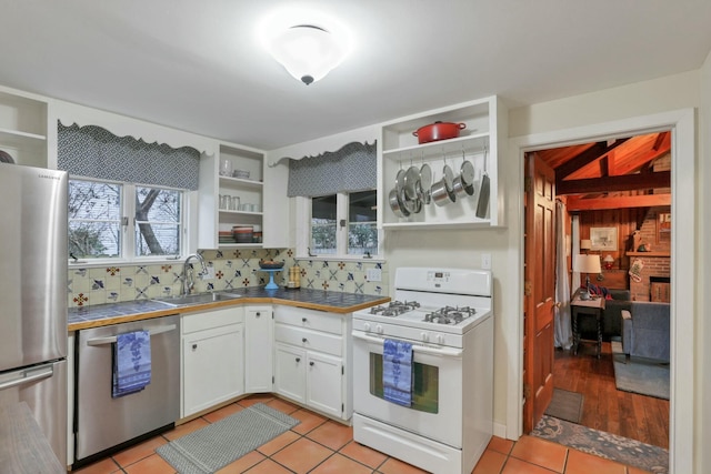 kitchen featuring stainless steel appliances, sink, light tile patterned floors, white cabinets, and tile counters