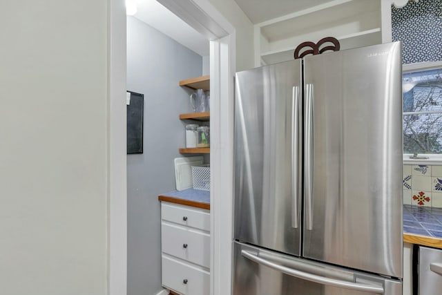 kitchen with decorative backsplash, stainless steel fridge, and white cabinetry