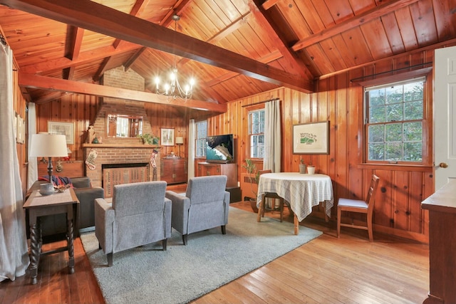 living room with a notable chandelier, lofted ceiling with beams, wood walls, and light hardwood / wood-style floors