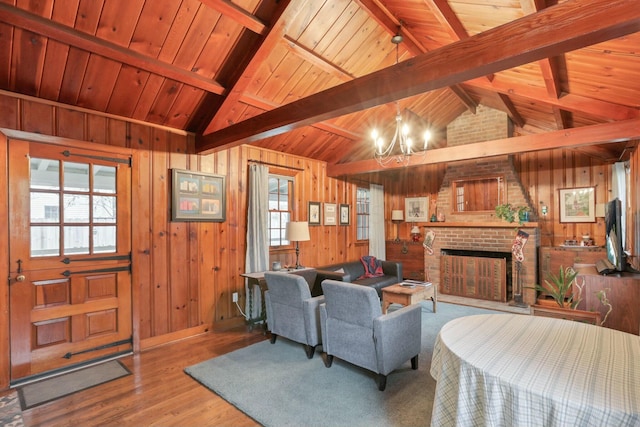 living room with an inviting chandelier, lofted ceiling with beams, wooden walls, a brick fireplace, and light hardwood / wood-style flooring