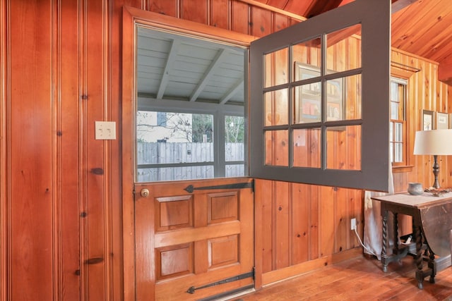 doorway to outside with lofted ceiling with beams, light hardwood / wood-style floors, wooden walls, and wood ceiling