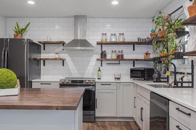 kitchen with butcher block counters, wall chimney range hood, backsplash, white cabinets, and black appliances