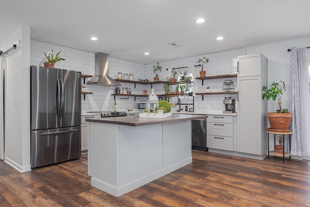 kitchen featuring appliances with stainless steel finishes, dark hardwood / wood-style flooring, wall chimney range hood, a barn door, and a kitchen island