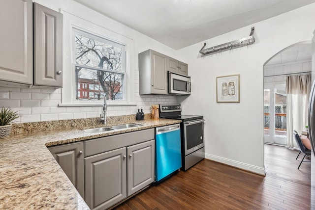 kitchen with dark wood-type flooring, sink, gray cabinets, stainless steel appliances, and light stone countertops