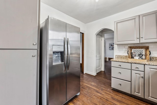 kitchen with gray cabinets, tasteful backsplash, stainless steel refrigerator with ice dispenser, light stone countertops, and dark wood-type flooring