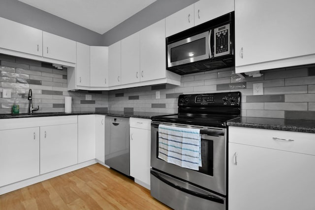 kitchen with stainless steel appliances, light hardwood / wood-style floors, white cabinets, dark stone counters, and sink