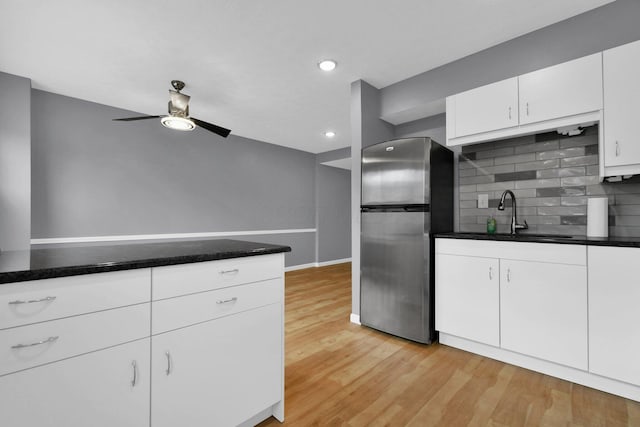 kitchen featuring sink, white cabinetry, light hardwood / wood-style floors, decorative backsplash, and stainless steel fridge