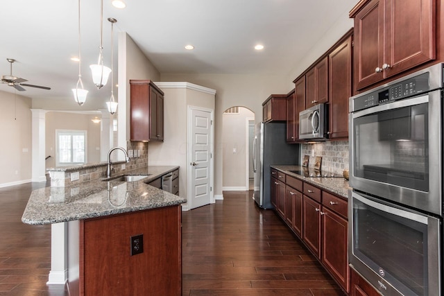 kitchen featuring backsplash, hanging light fixtures, sink, dark stone countertops, and appliances with stainless steel finishes