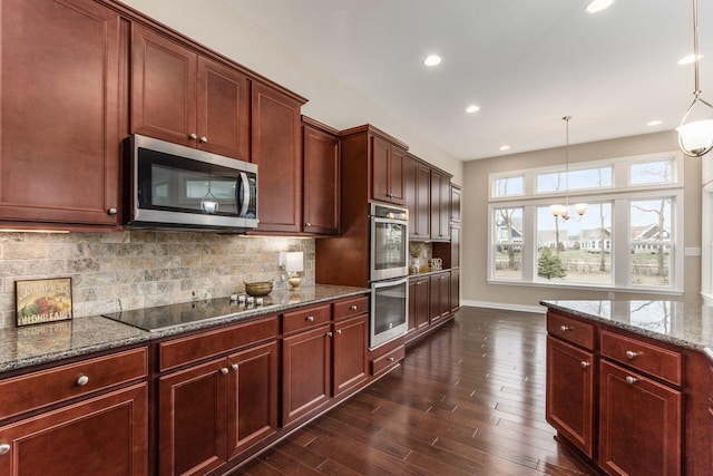 kitchen with dark stone counters, dark hardwood / wood-style floors, decorative light fixtures, stainless steel appliances, and a chandelier