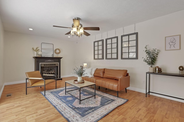 living room featuring ceiling fan, light wood-type flooring, and a textured ceiling