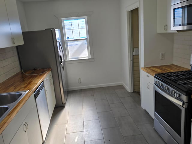 kitchen with tasteful backsplash, butcher block countertops, white cabinets, and appliances with stainless steel finishes