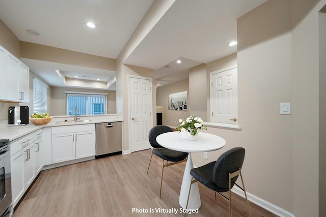 kitchen with sink, stainless steel dishwasher, a tray ceiling, light hardwood / wood-style floors, and white cabinetry