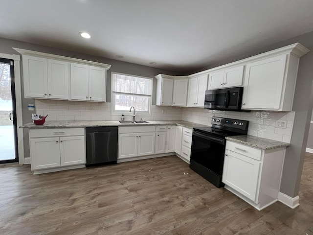 kitchen with dark wood-type flooring, black appliances, sink, plenty of natural light, and white cabinetry