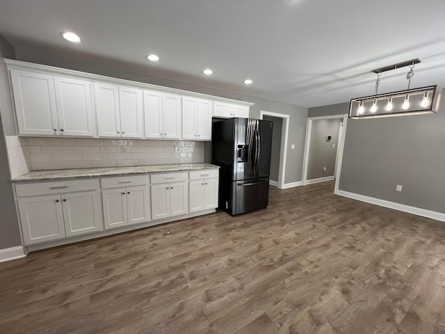 kitchen with light stone counters, refrigerator with ice dispenser, backsplash, pendant lighting, and white cabinets