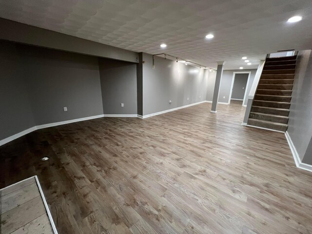 basement featuring rail lighting and light hardwood / wood-style flooring