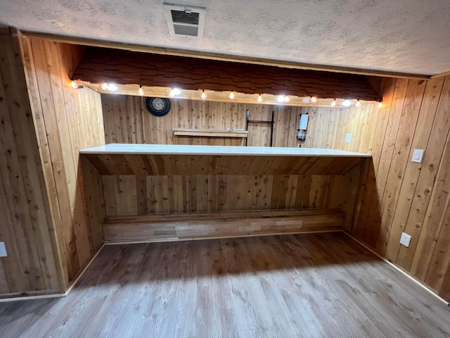 bar with a textured ceiling, hardwood / wood-style flooring, and wooden walls