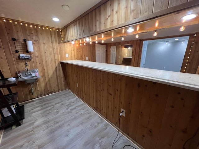 bar featuring wood walls, sink, and light wood-type flooring