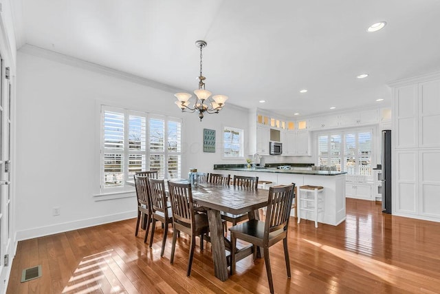 dining area with hardwood / wood-style floors, a notable chandelier, sink, and crown molding