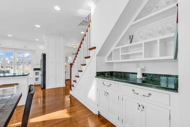 bar with white cabinets, wood-type flooring, and stainless steel refrigerator