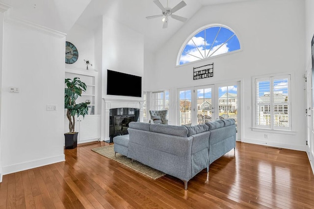 living room with hardwood / wood-style floors, ceiling fan, built in features, and high vaulted ceiling