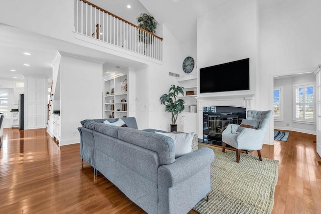 living room with built in shelves, a towering ceiling, and hardwood / wood-style flooring