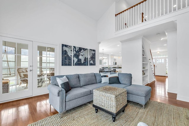 living room featuring built in shelves, high vaulted ceiling, wood-type flooring, and a notable chandelier