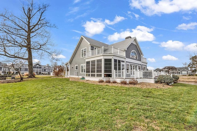 rear view of property featuring a lawn, a sunroom, and a balcony