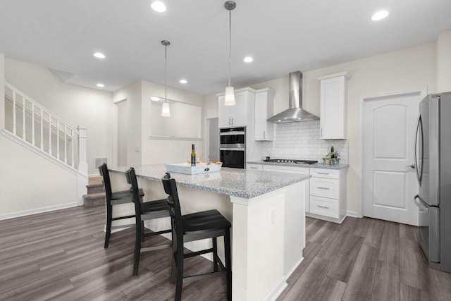 531 White Fawn Run, Delaware, OH 43015 - kitchen with wall chimney exhaust hood, appliances with stainless steel finishes, dark wood-type flooring, white cabinetry, and light stone counters