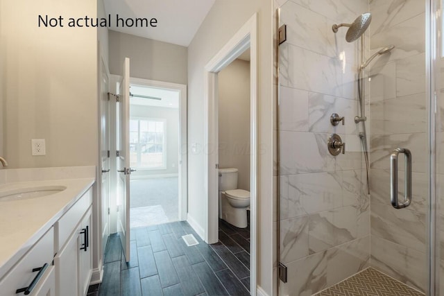 bathroom featuring toilet, a stall shower, wood tiled floor, and vanity