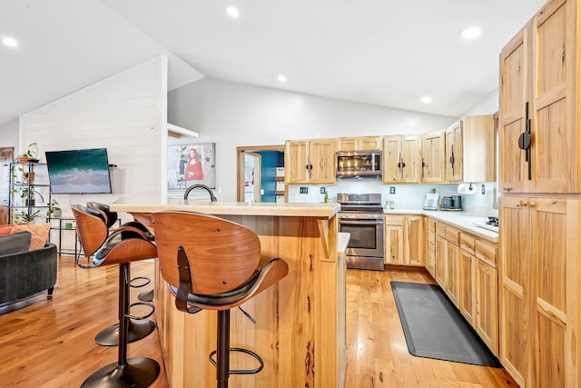 kitchen featuring a center island, a kitchen breakfast bar, light hardwood / wood-style floors, light brown cabinetry, and appliances with stainless steel finishes