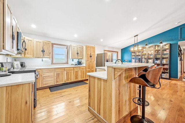 kitchen with vaulted ceiling, stainless steel fridge with ice dispenser, hanging light fixtures, a breakfast bar area, and an island with sink