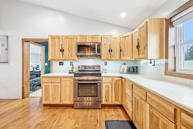 kitchen with appliances with stainless steel finishes, light brown cabinets, light hardwood / wood-style flooring, and lofted ceiling