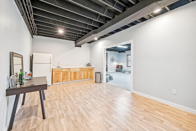 basement with white fridge, light wood-type flooring, and sink