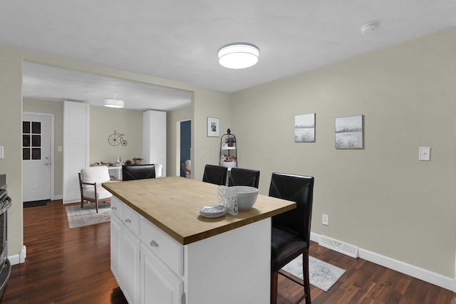 kitchen featuring a breakfast bar, wood counters, dark hardwood / wood-style floors, a kitchen island, and white cabinetry