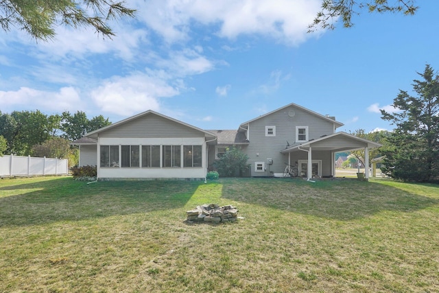 rear view of property featuring a lawn, a sunroom, and an outdoor fire pit