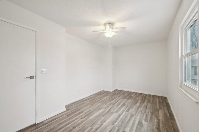 empty room featuring ceiling fan, a wealth of natural light, a textured ceiling, and light hardwood / wood-style flooring