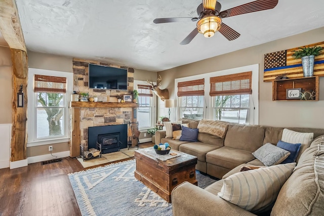 living room with ceiling fan, a wood stove, and dark wood-type flooring