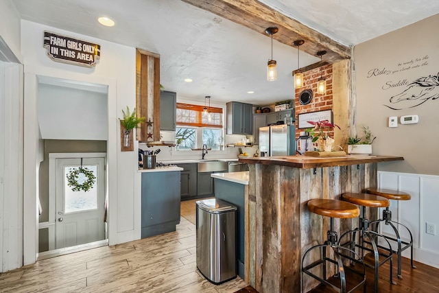 bar with gray cabinetry, sink, light hardwood / wood-style flooring, stainless steel fridge with ice dispenser, and hanging light fixtures