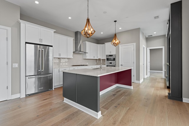 kitchen with stainless steel appliances, a sink, light countertops, wall chimney exhaust hood, and tasteful backsplash