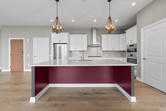 kitchen featuring stainless steel appliances, a sink, wall chimney range hood, and light wood-style flooring